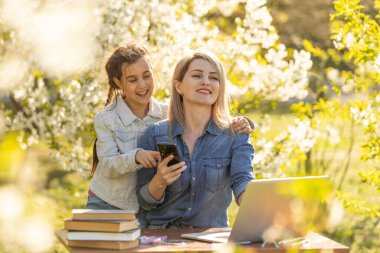 Anne kızı dışarıda vakit geçiriyor. Anne ve çocuk doğada laptop kullanıyorlar..