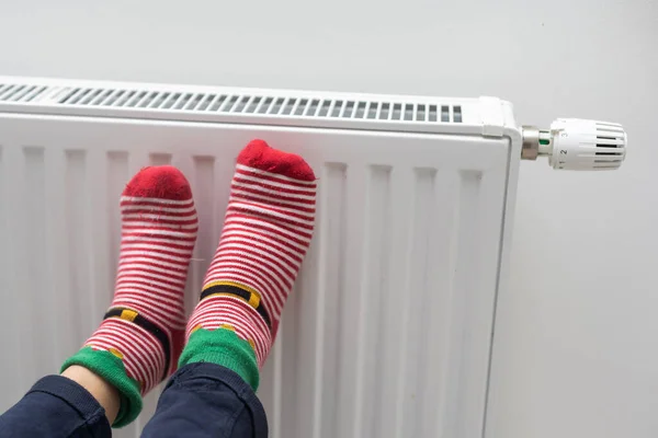 Persons feet in bright winter socks near heating radiator at home.