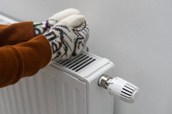 Closeup of woman warming her hands on the heater at home during cold winter days, top view. Female getting warm up her arms over radiator. Concept of heating season, cold weather