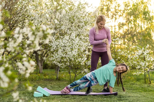 Young sports mother doing physics exercise outdoors in garden near her daughter. Healthy lifestyle. Yoga. Fitness. Family having fun outside. Family spend time together in park