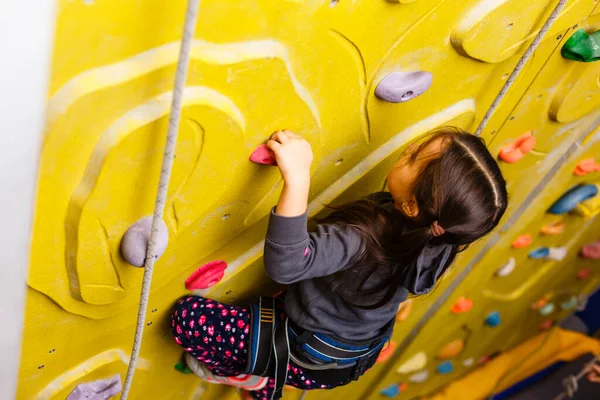 little girl climbing a rock wall indoor
