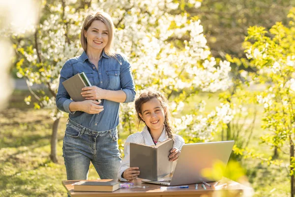 Beautiful mom with little daughter resting with a laptop in the park on a sunny day. Study, Learning, harmony, happiness, paradise - concept.