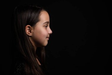 Profil yan görüntüsü. Siyah stüdyo arka planında yalnız duran kahverengi saçlı küçük kız..