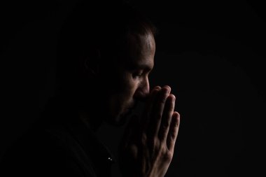 Elleri sıkıca bağlı siyah arka planda dua eden adam..