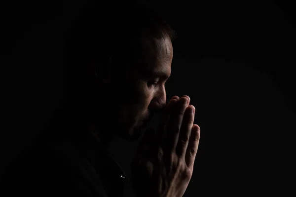 Man with clasped hands praying on black background.