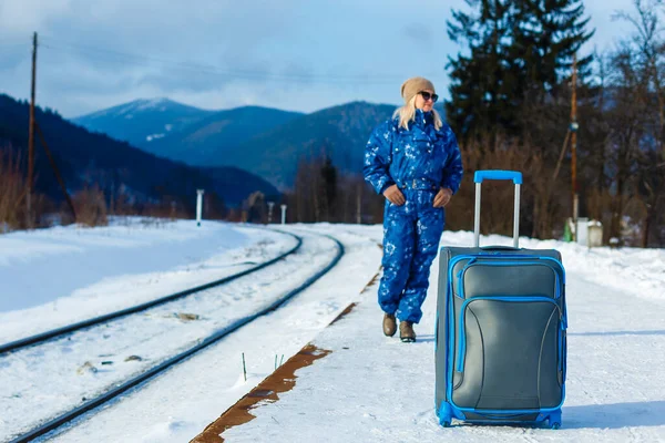 Woman pulling heavy luggage at a snow train station. Travelling by train at winter