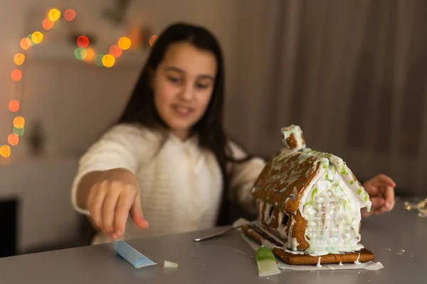 Little girl decorating gingerbread house for Christmas.