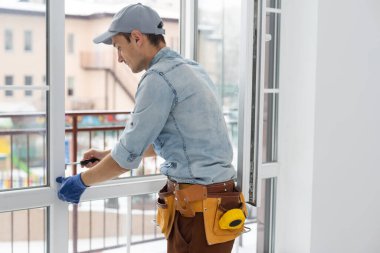 Yakışıklı genç adam yeni bir inşaat alanına pencere takıyor.