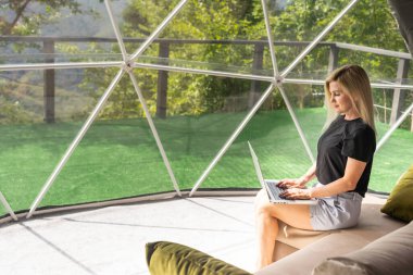 Kafkasyalı genç bir kadın, kubbe kamp otelinde dizüstü bilgisayarını kullanıyor ve izliyor. Turizm, tatil ve hafta sonu