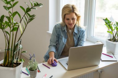 Laptop ekranına bakıp gülümseyen genç bir kadın, mesajda iyi haberler okuyor, video izliyor, sosyal ağda sohbet ediyor ya da evde online alışveriş yapıyor, bilgisayarla boş vakitlerin keyfini çıkarıyor.