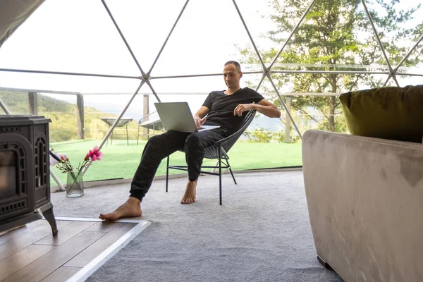 a man works on a laptop in a dome tent.