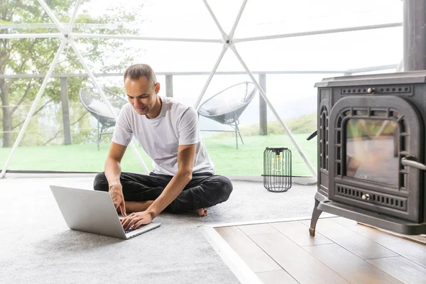 a man works on a laptop in a dome tent.