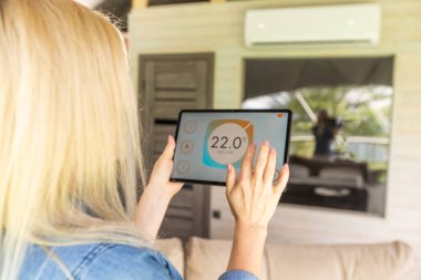 Akıllı tabletle akıllı ev uygulaması olan eller arka plan olarak ev oturma odasında..