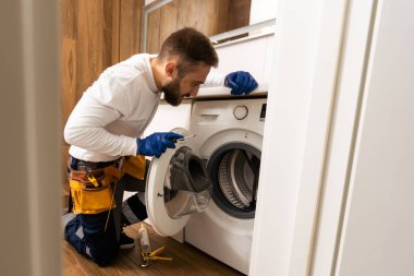 Tulumlu tesisatçı, evdeki çamaşır makinesini tamir ediyor.