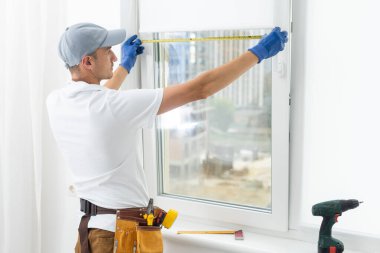 Using drill by installing windows. Repairman is working indoors in the modern room.