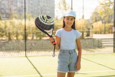 little girl with racket playing padel tennis at court.