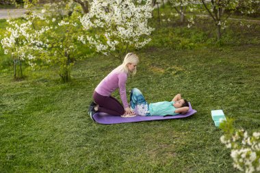 Genç bir anne ve kız, parkta spor minderinin üzerinde yoga egzersizleri yapıyorlar. sağlıklı yaşam tarzı