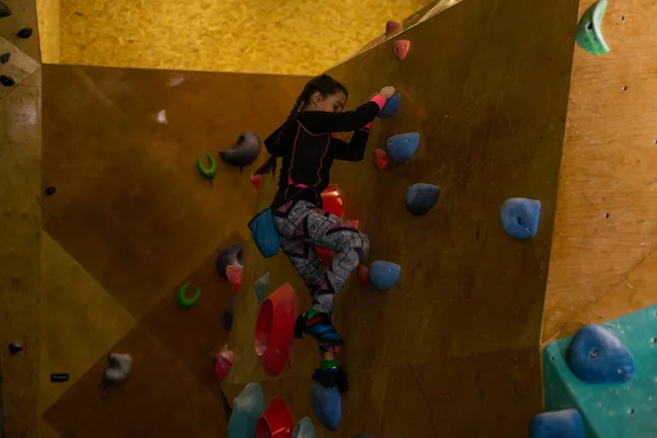 little girl climbing a rock wall indoor.