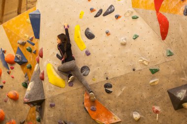 Girl climbing on practical wall indoor, bouldering training.