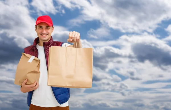 Young Delivery Man Carrying Cardboard Box In Front Of sky background.