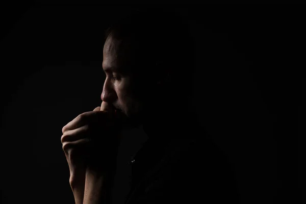 Man with clasped hands praying on black background.