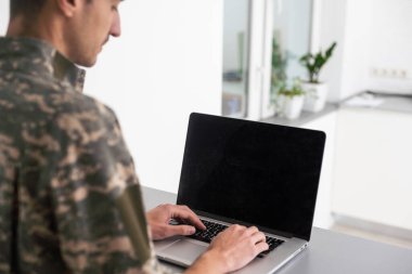 Askeri üniformalı adam dizüstü bilgisayara bakıyor..