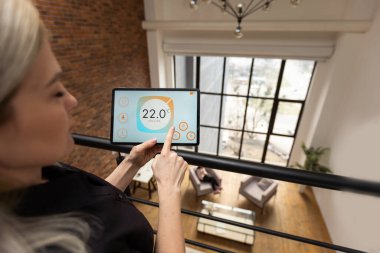 young woman using smart home app to control light turning on with tablet pc.