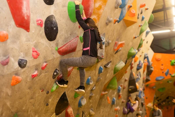 Girl climbing on practical wall indoor, bouldering training.