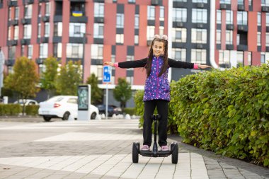 Elektrikli scooter kullanan küçük bir kız. Kişisel çevre taşımacılığı, jiroskoplu scooter, akıllı denge çarkı. Popüler elektrik taşımacılığı.