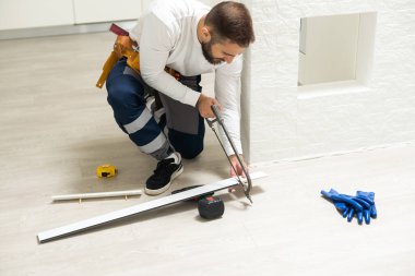 The craftsman measures the length of the plinth for cutting, installing the plinth on the corner of the wall, close-up installation.