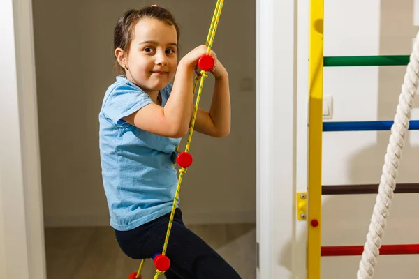 The girl smiles, plays and goes in for sports on the stairs and the Swedish wall in the childrens center in special tight clothes and leads a healthy lifestyle under the supervision of her parents.