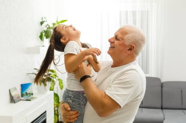 Cute little girl spending time with positive active grandpa in living room.
