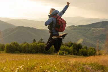 Sırt çantalı bir turist sırtında sırt çantasıyla dağlarda duruyor..