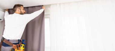 İşçi tamirci penceredeki perdeyi asıp tamir ediyor..