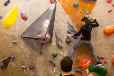 Sportif küçük kız spor salonunda yapay kayaya tırmanıyor..