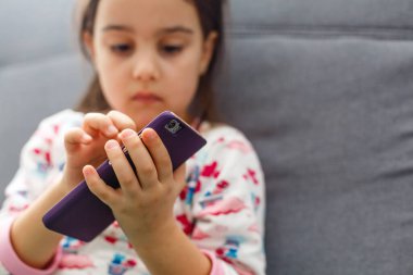 Güzel küçük kız oyun oynuyor ya da akıllı telefondan video izliyor. Çizgi film izleyen, internette gezinen, fotokopi çeken bir kız. Akıllı telefon kullanan küçük bir kızın yan görünüm portresi.