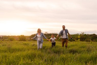 Park akşam ışığında mutlu bir aile. Güneşin ışıkları. Anne, baba ve bebek gün batımında mutlu yürüyüşler. Mutlu aile kavramı..