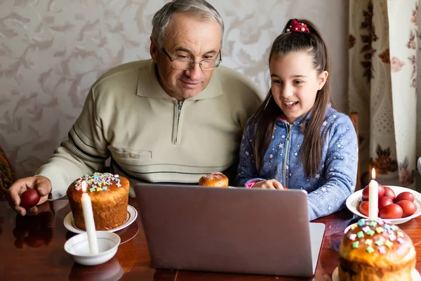 grandfather and granddaughter using laptop on kitchen, online, video call to friends, easter at home during coronavirus covid-19 outbreak