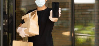 Müşteri evinin yakınında koruyucu maskeli bir teslimatçı.