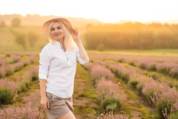 Lavanta tarlasında saman şapkalı genç sarışın gezgin lavanta çiçekleriyle çevrili.