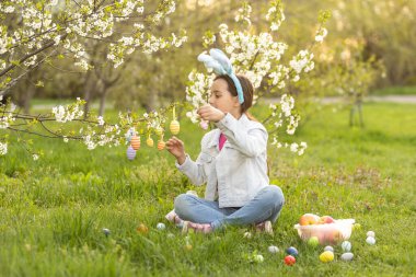 Küçük kız tavşan kulağı takıyor ve bahar günü dışarıda renkli Paskalya yumurtaları var..