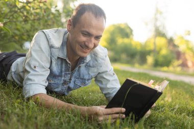 Genç adam çimenlerde uzanıyor, rahatlıyor ve kitap okuyor..