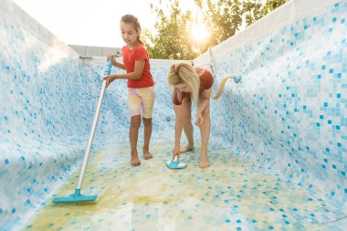 Anne ve kızı bahçede yüzme havuzu temizliyor.