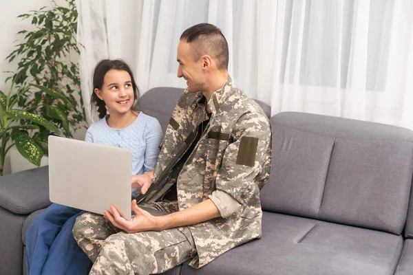 Happy military man smiling and hugging his family while using laptop indoors.