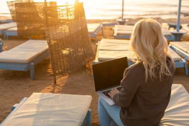 Deniz kıyısında uzaktan çalışıyor. Günbatımında tropikal plajda tam uzunlukta otururken hasır şapkalı başarılı kadın serbest yazar. Mesafe çalışma kavramı