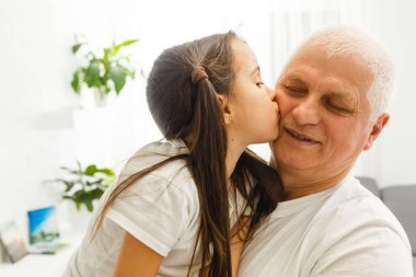 Komik iki kişinin fotoğrafı. Yaşlı büyükbaba, küçük torun rahat koltukta oturup güzel bir hikaye anlatıyor. Ev karantinası, güvenlik, modern tasarım iç mekan.