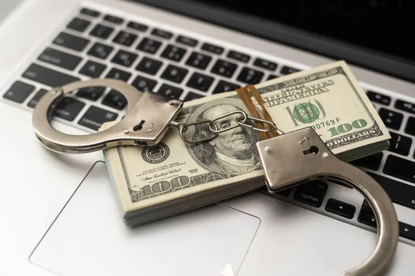 Cyber crime legal law police handcuffs on a hundred dollar bills with computer keyboard technology of criminal taking fingerprint on paper.