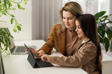 Genç kız, mutfakta annesiyle ders çalışıyor. Ergen kız öğrenci mesafesi, uzaktan eğitim sırasında birlikte ev ödevi yapmaya yardım eden anne ya da öğretmenle sanal ders öğreniyor..