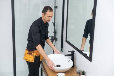 Contemporary technician in workwear installing pipe system by bathtub. High quality photo