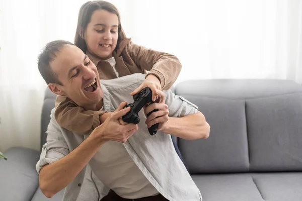 family, gaming and entertainment concept - happy father and little daughter with gamepads playing video game at home.